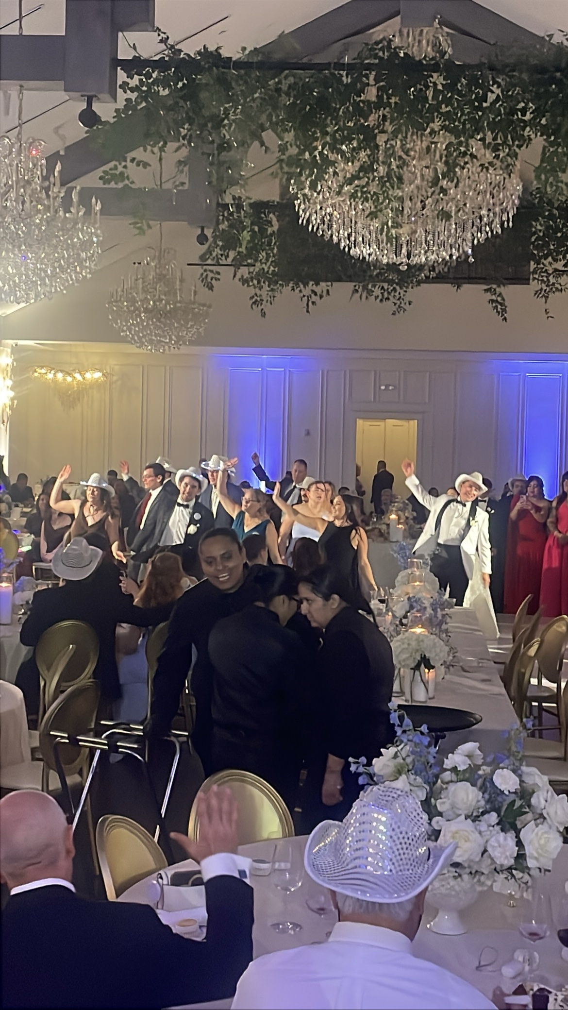 Wedding guests dancing in white cowboy hats under chandeliers